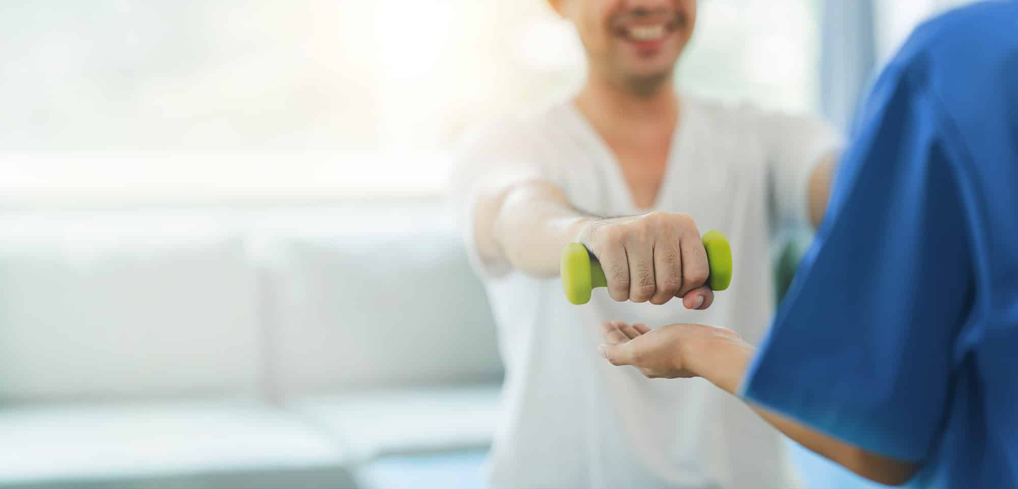 Smiling patient performing arm strength rehabilitation exercise with a dumbbell under the guidance of a physiotherapist in a clinical setting